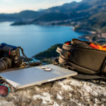 a laptop, camera and bag for how to start a travel blog