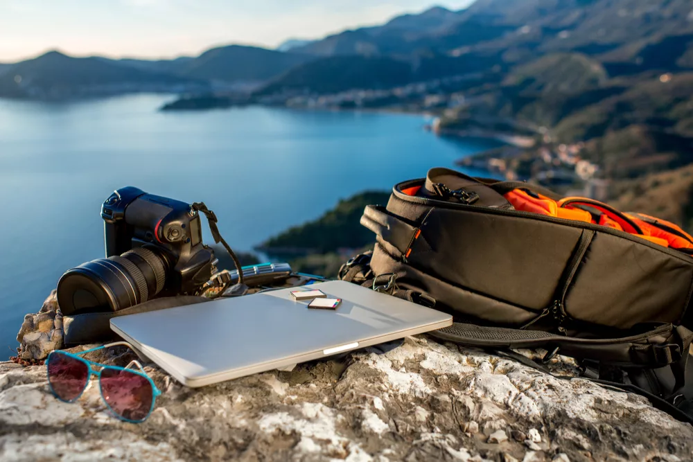 a laptop, camera and bag for how to start a travel blog