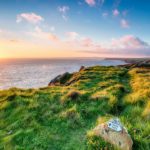 The sun sets over the sea on a section of the English coast. A trail sign is seen in the foreground.