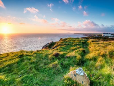 The sun sets over the sea on a section of the English coast. A trail sign is seen in the foreground.