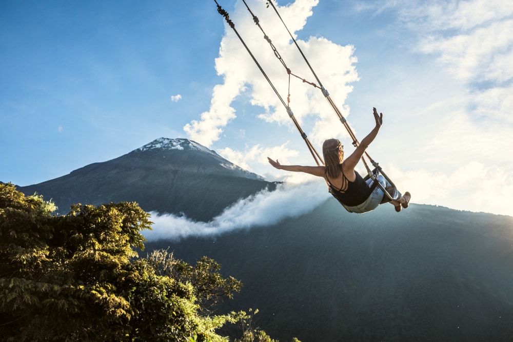A woman swings with the volcano smoking in the background