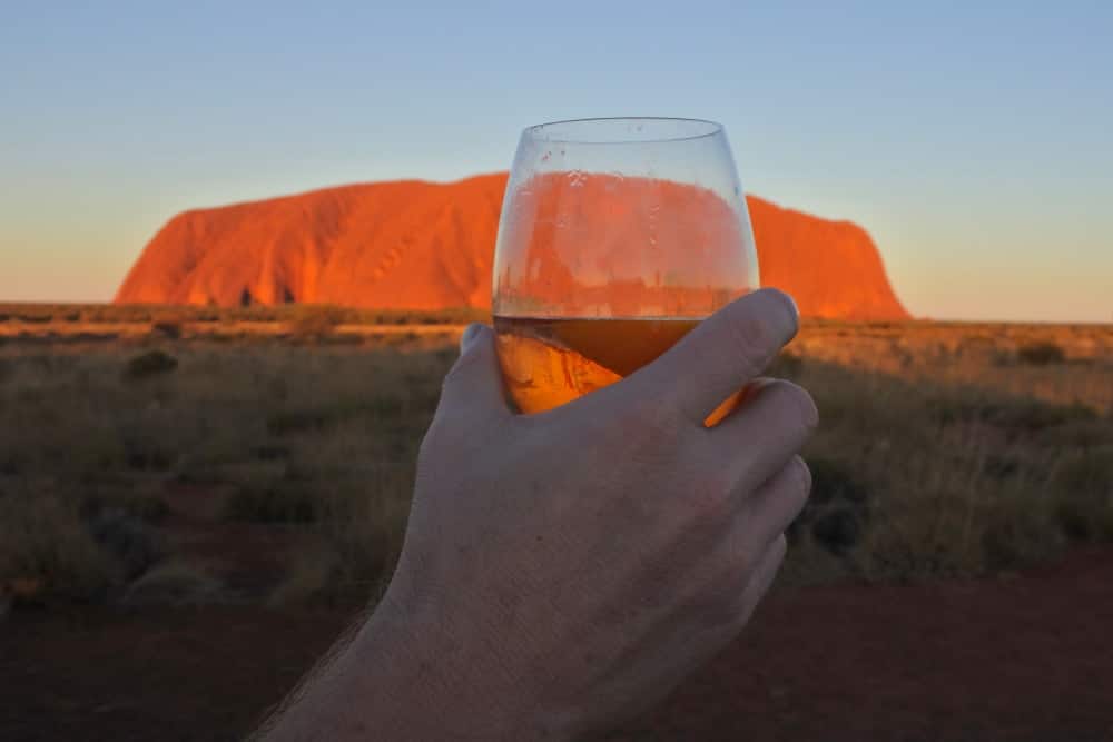 A glass of wine being raised in front of Uluru