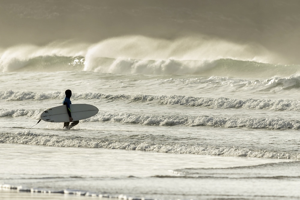A surfer on Fistral Beach approaches the waves