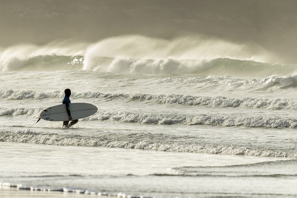 Seorang peselancar memukul ombak di Pantai Fistral