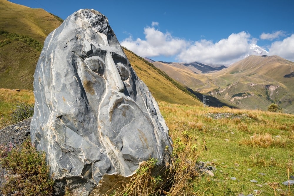 A stone face in a field with mountains in the background at the village of Sno