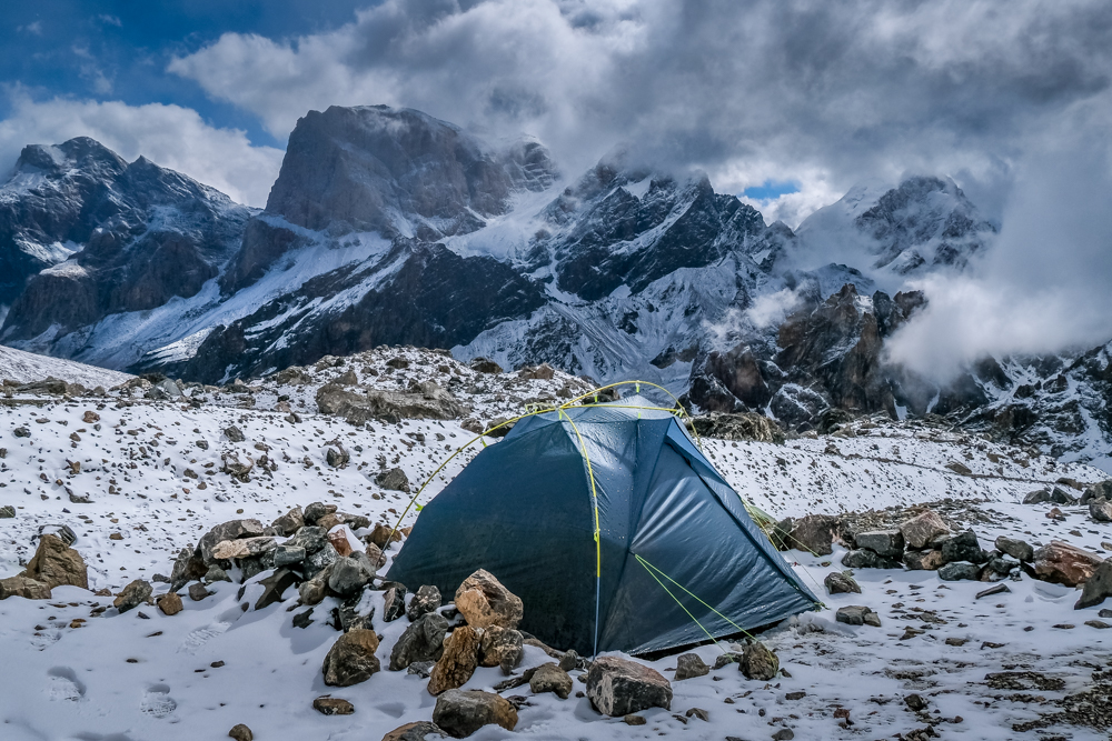 A tent surrounded by snow and rocks in the Fann Mountains