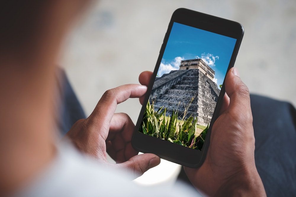 A man holding a smartphone with a photo of Chichén Itzá in Mexico