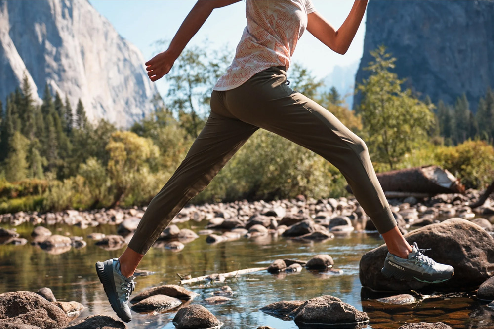 A woman hops across a stream in the jogging bottoms