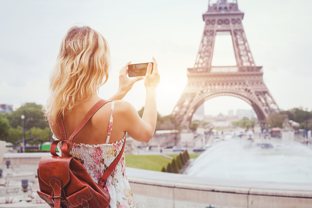 A woman takes a photo on her phone in Paris, one of the best cities to visit in Europe