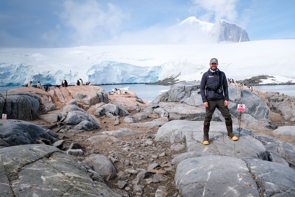 Peter next to a penguin study sign at Port Lockroy, one of the best antarctic destinations
