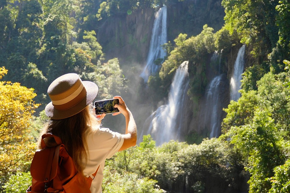 woman taking photo of a waterfall in thailand